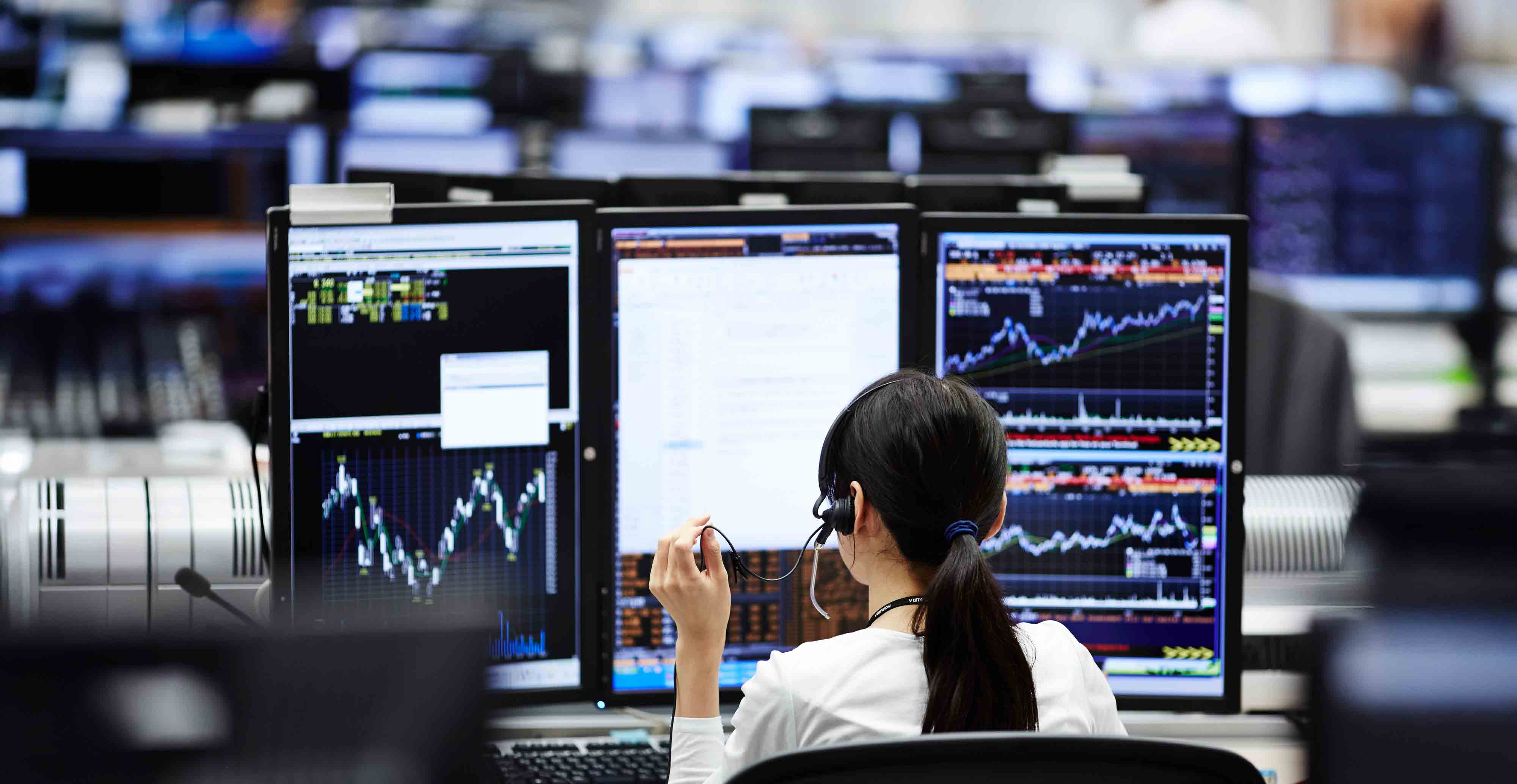 Women sits at trading desk analyzing financial trendlines on a computer screen